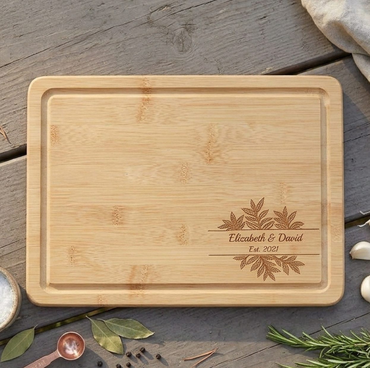 Personalized anniversary cutting board with laurel design and engraved couple's names on a rustic wood table.