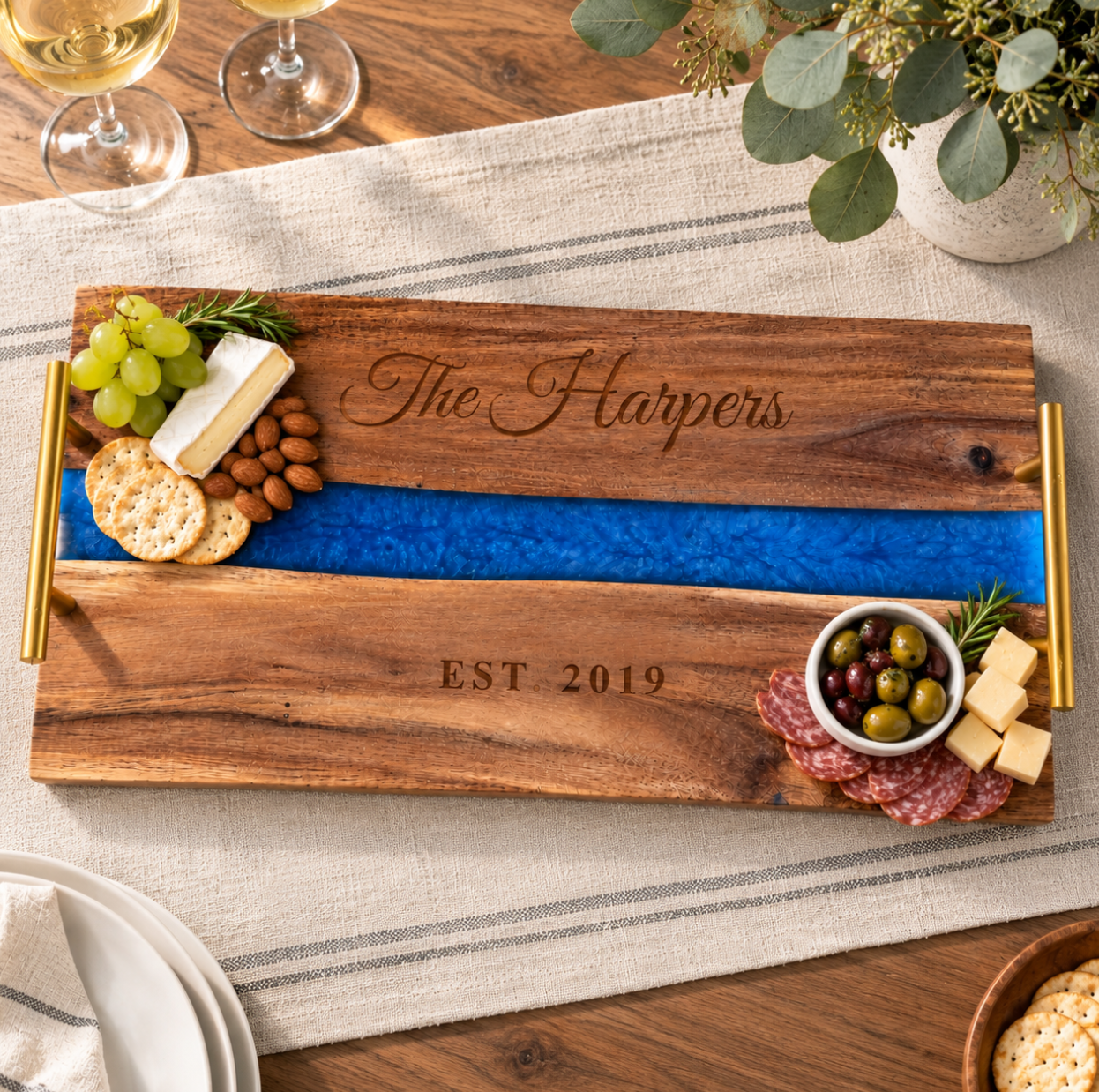 Personalized river serving tray engraved The Harpers and EST. 2019 with grapes, brie, crackers, almonds, olives and salami on a dining table with white wine