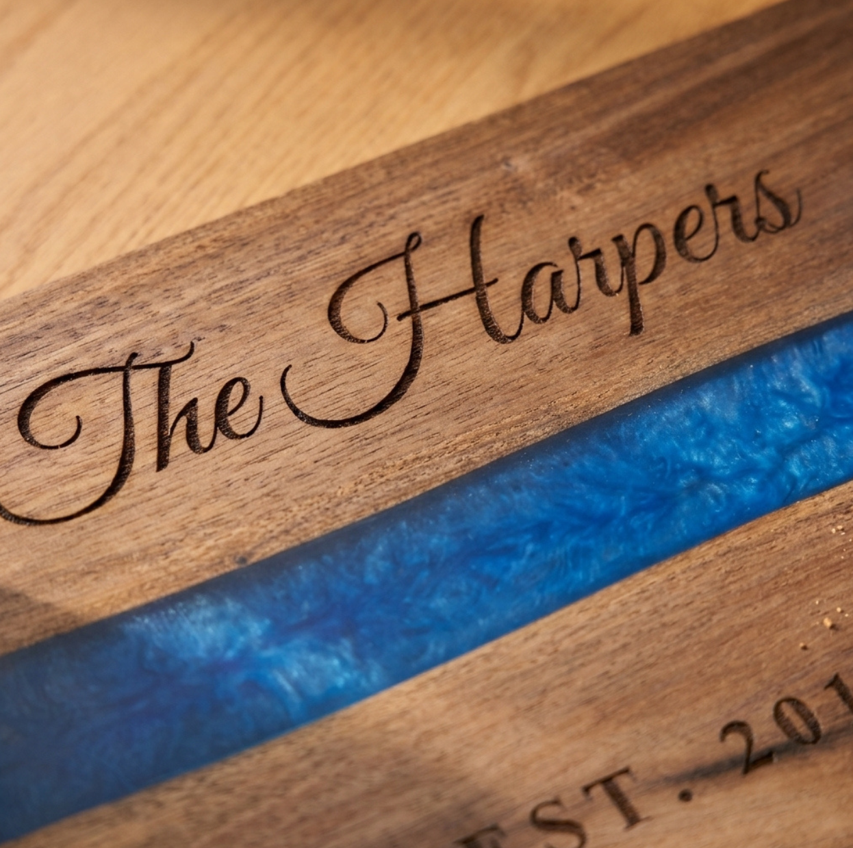 Close-up of the laser engraving on the acacia serving tray: The Harpers in flowing script burned into the wood above the blue pearl resin river