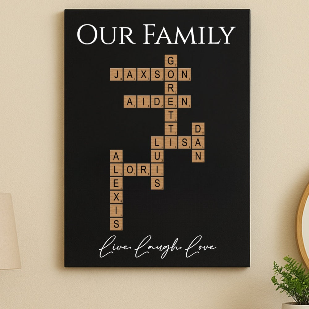 Black wood sign with "Our Family" header and Scrabble-style tiles forming a crossword with sample names Jaxson, Grayson, Aiden, Lisa, Lori, and Alexis, with "Live Laugh Love" script at bottom.