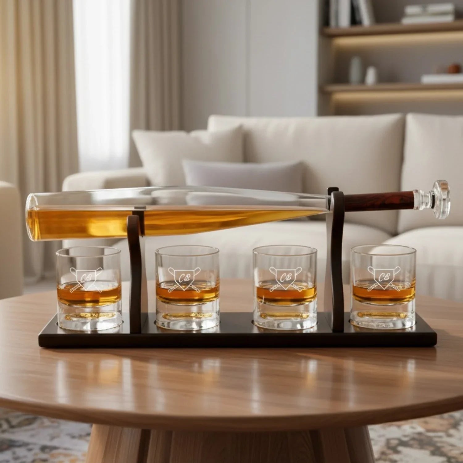 Whiskey decanter set with bat-shaped bottle filled with amber liquid, dark wood base, and four glasses engraved with sample initials "CB" and baseball design, displayed on round wooden table