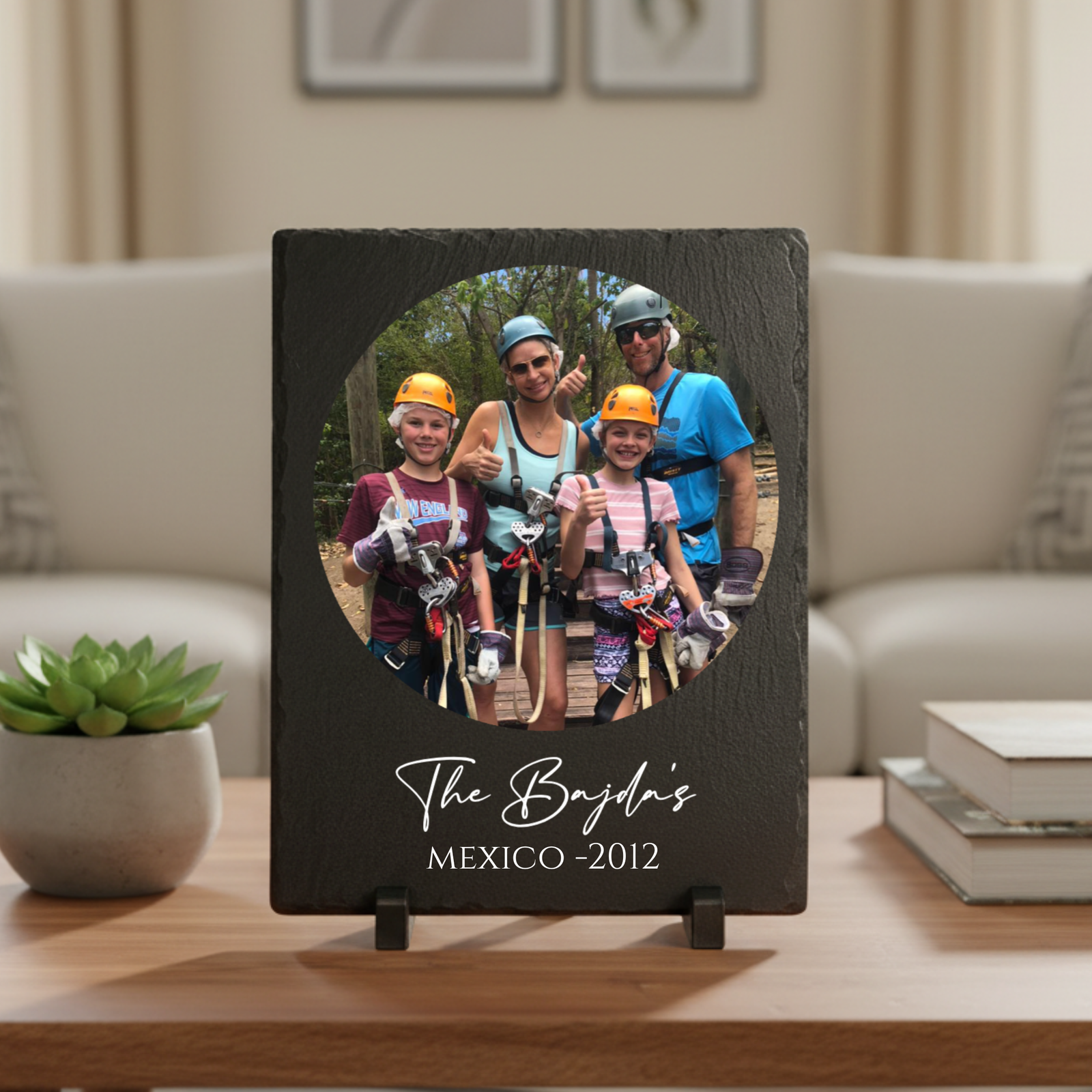 Black slate plaque with circular photo cutout displaying a family of four in safety gear, engraved below with sample text "The Boyds" and "MEXICO -2012", displayed on wooden stand.
