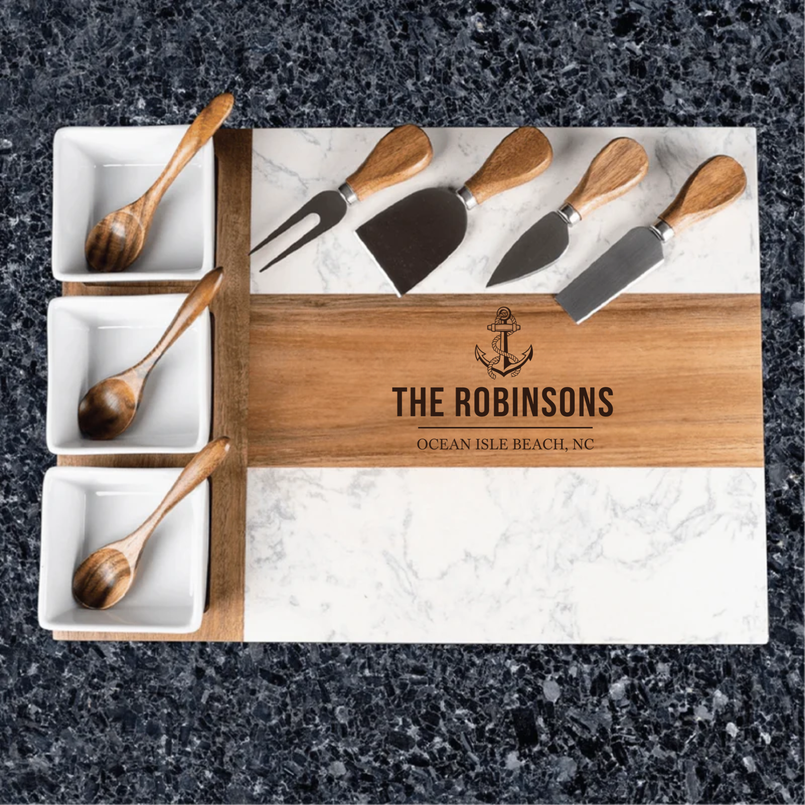 Engraved charcuterie board with sample text "THE ROBINSONS" and "OCEAN ISLE BEACH, NC" displayed with marble surface, wooden accents, cheese knives, and small white serving bowls