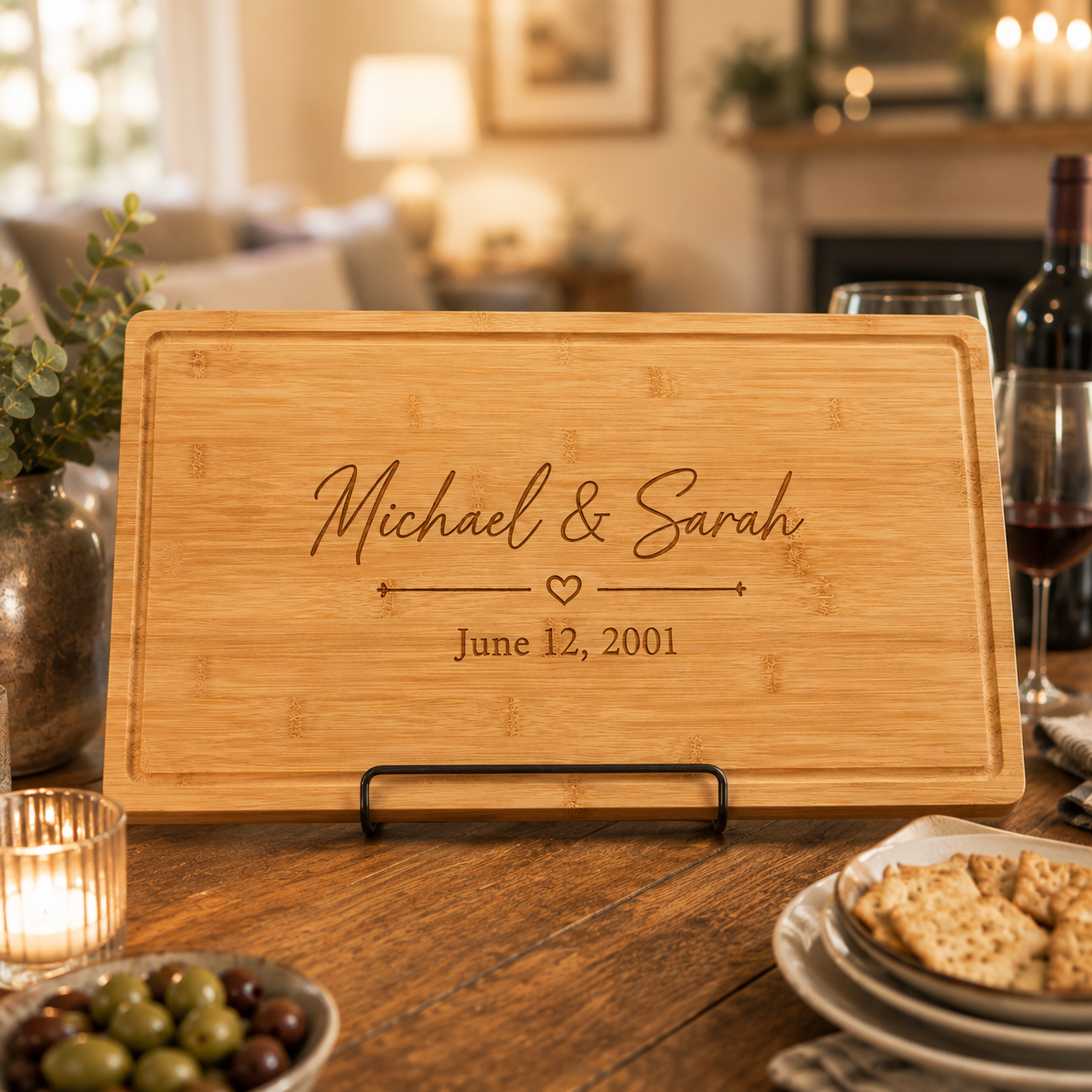 Personalized wedding serving board engraved with Michael & Sarah, a heart and June 12, 2001, standing on a dining table with candles, wine and crackers