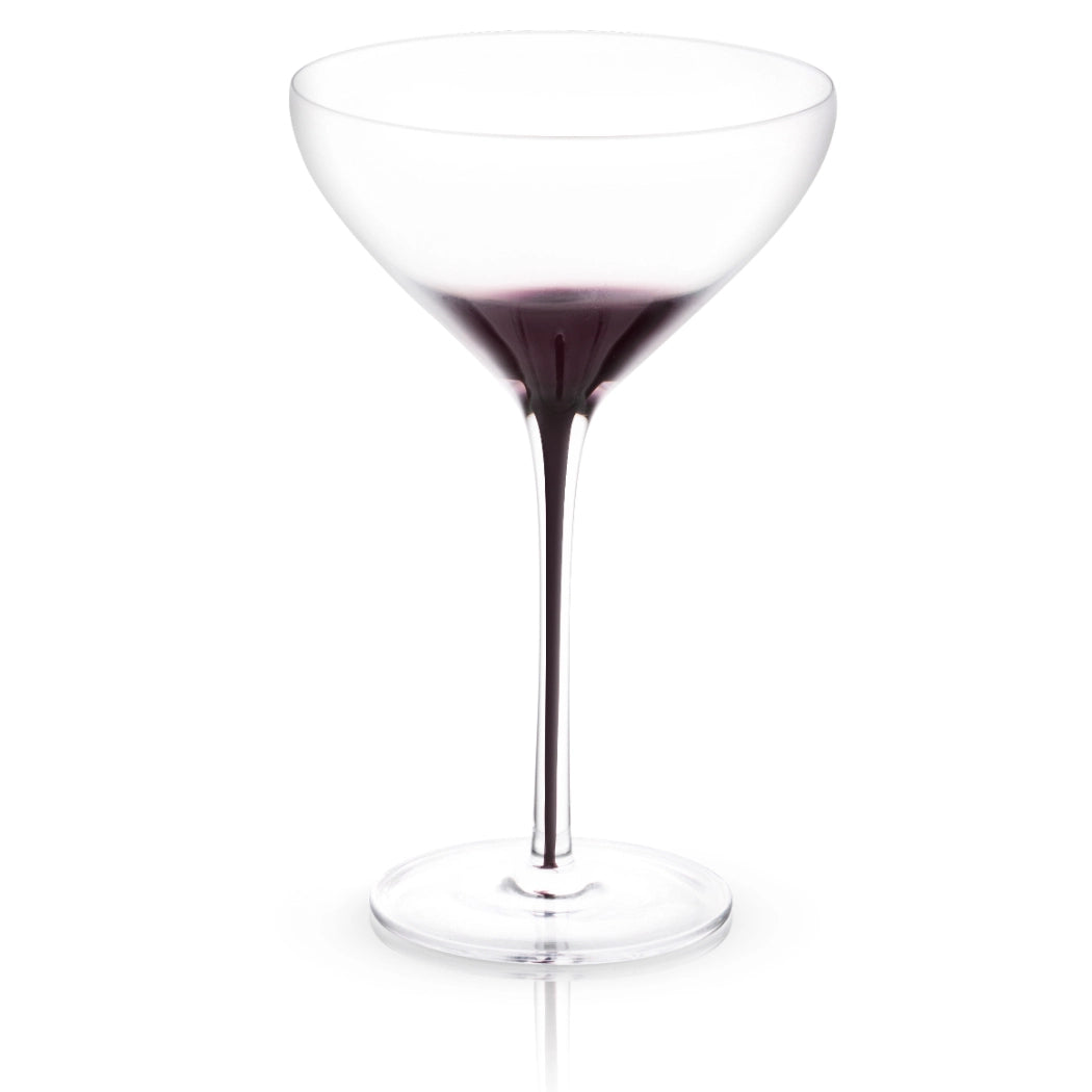 Clear martini glass with black swan-shaped stem, filled with dark purple cocktail, shown against white background