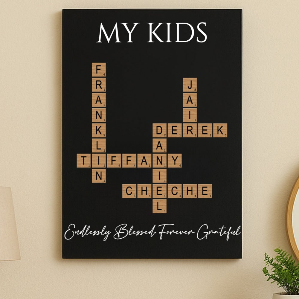 Black wall art with "MY KIDS" header and crossword layout featuring sample names Frank, Tiffany, Derek, and Cheche in wooden tile letters, with cursive text reading "Endlessly Blessed Forever Grateful" at bottom.