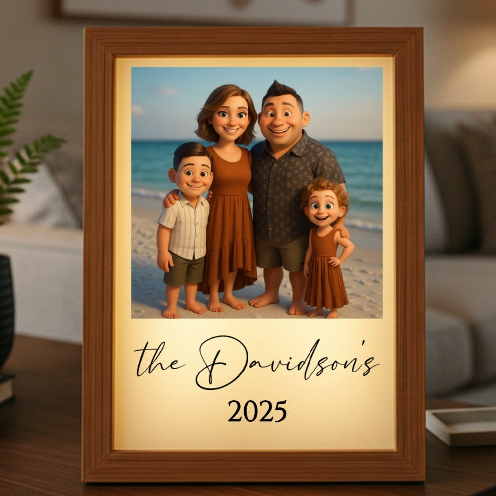 Framed light box displaying animated family portrait on beach with sample text "the Davidsons" and "2025" on cream-colored mat, wood frame displayed on wooden surface