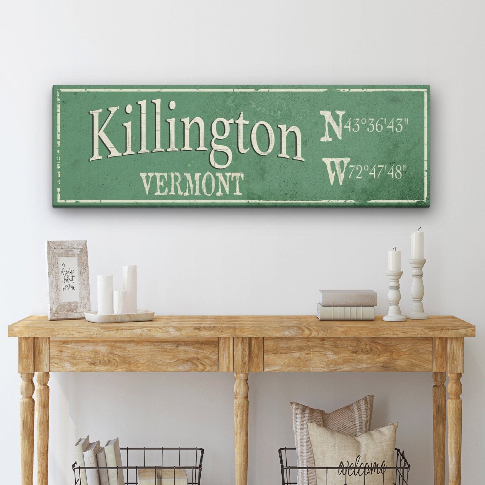 Personalized hometown canvas sign in sage green with cream text displaying "Killington" and "Vermont" with GPS coordinates, styled on wooden console table with home décor accents