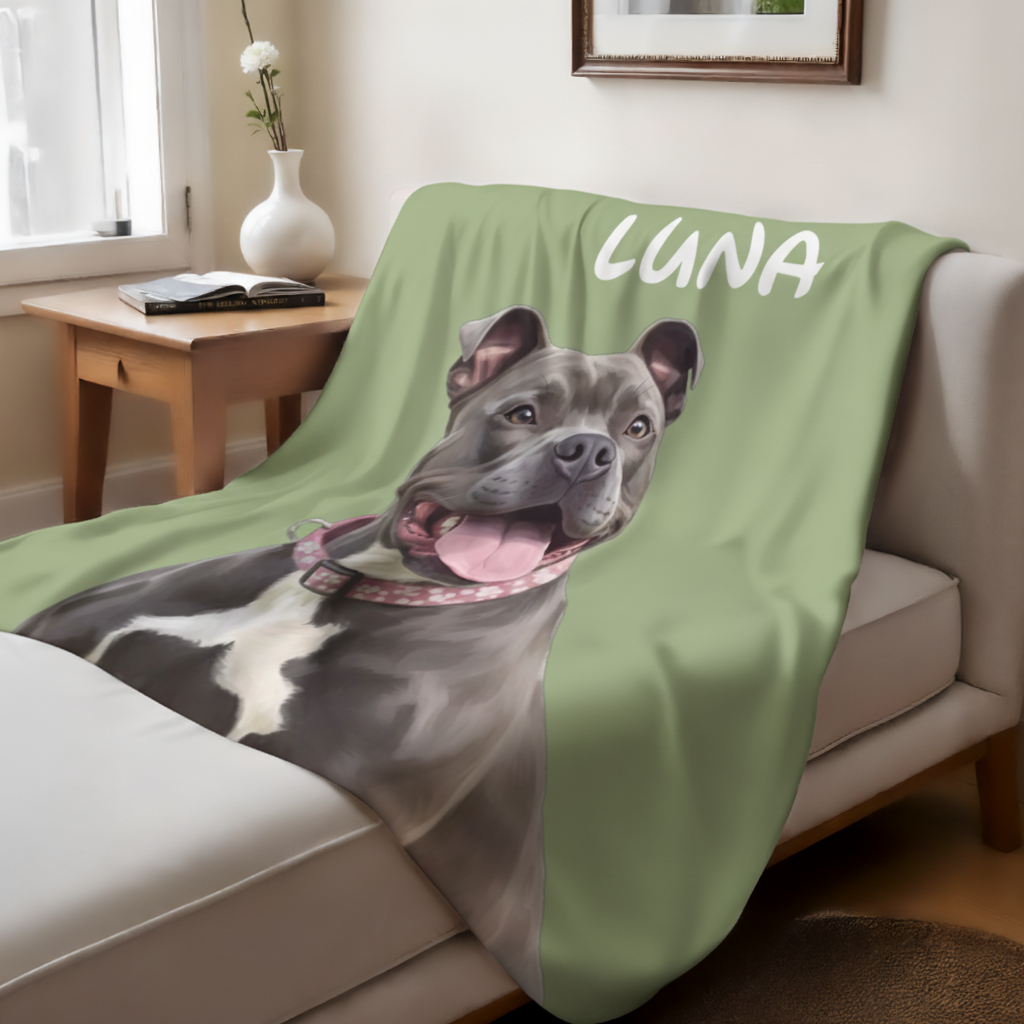 Sage green sherpa blanket draped over a couch, printed with a cartoon portrait of a smiling French Bulldog and the sample name "LUNA" in white lettering
