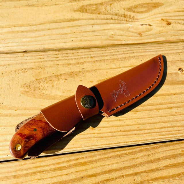 Brown leather sheath with white stitching and snap closure, displayed next to fixed blade knife with wood handle on wooden surface