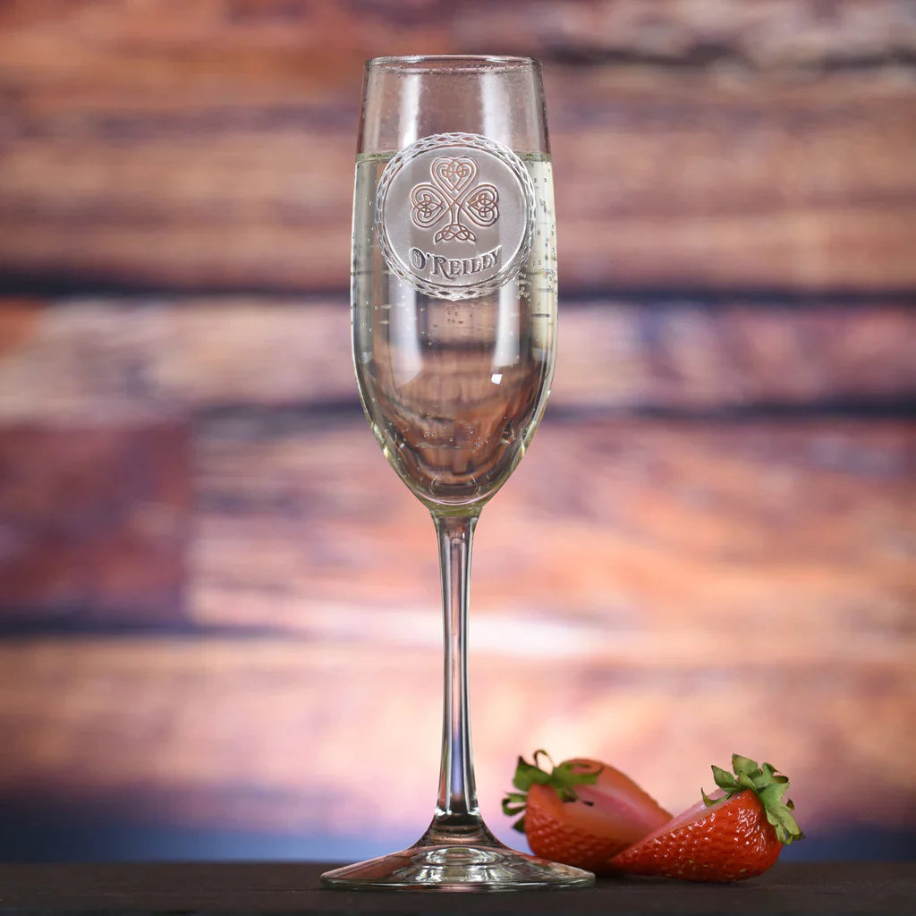 Champagne flute with sample engraving of Celtic shamrock design and "O'REILLY" name, filled with champagne and styled with fresh strawberries against wooden backdrop.