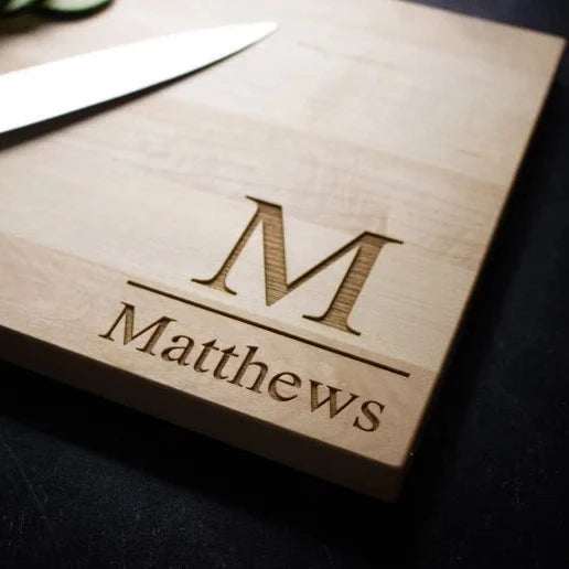 Wood cutting board engraved with sample monogram "M" and name "Matthews" in laser-etched lettering on natural wood surface