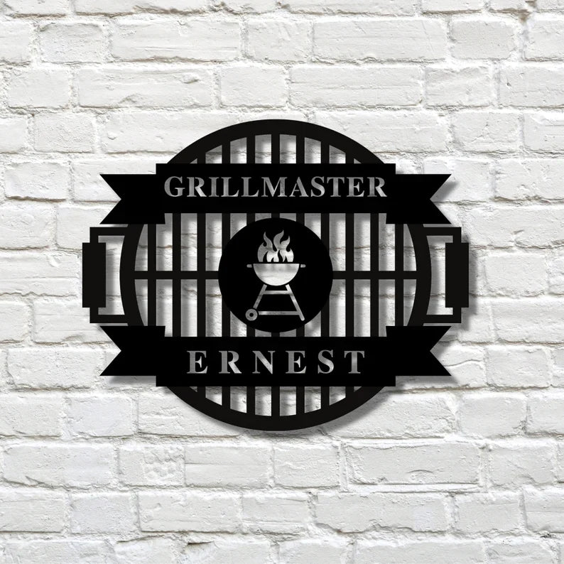 Black laser-cut metal grill master sign mounted on white brick wall, featuring grill icon and banner with sample personalization "GRILLMASTER" and "ERNEST