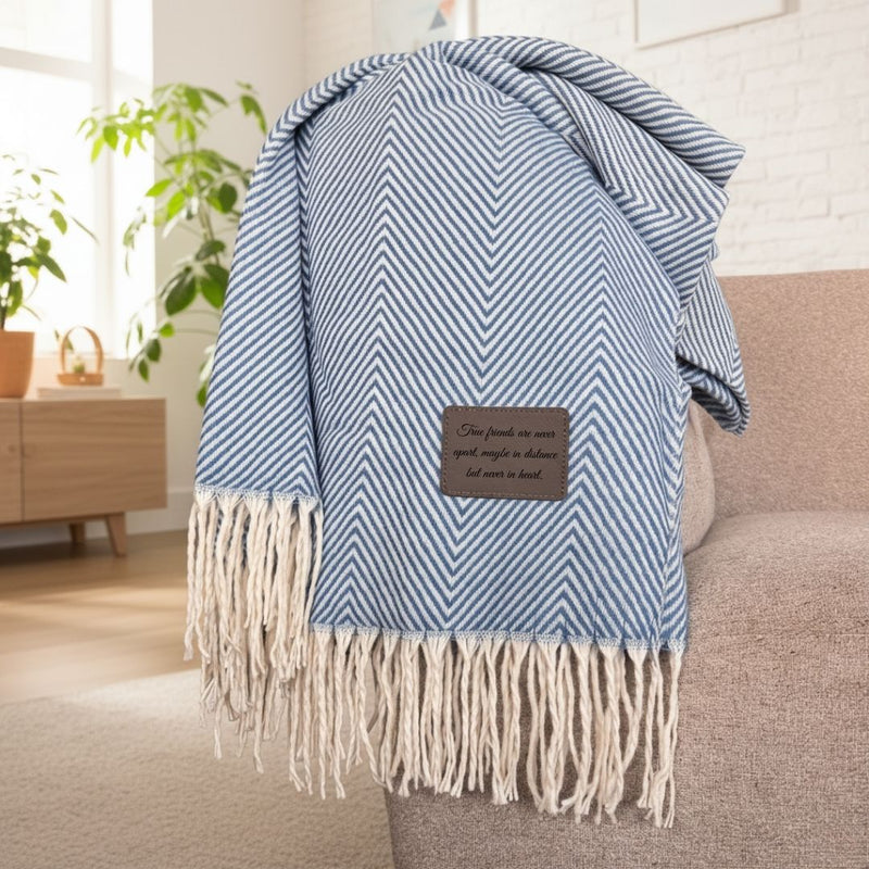 Blue and white chevron throw blanket draped over a chair, featuring a leather patch engraved with sample text "True friends are never apart, maybe in distance but never in heart.