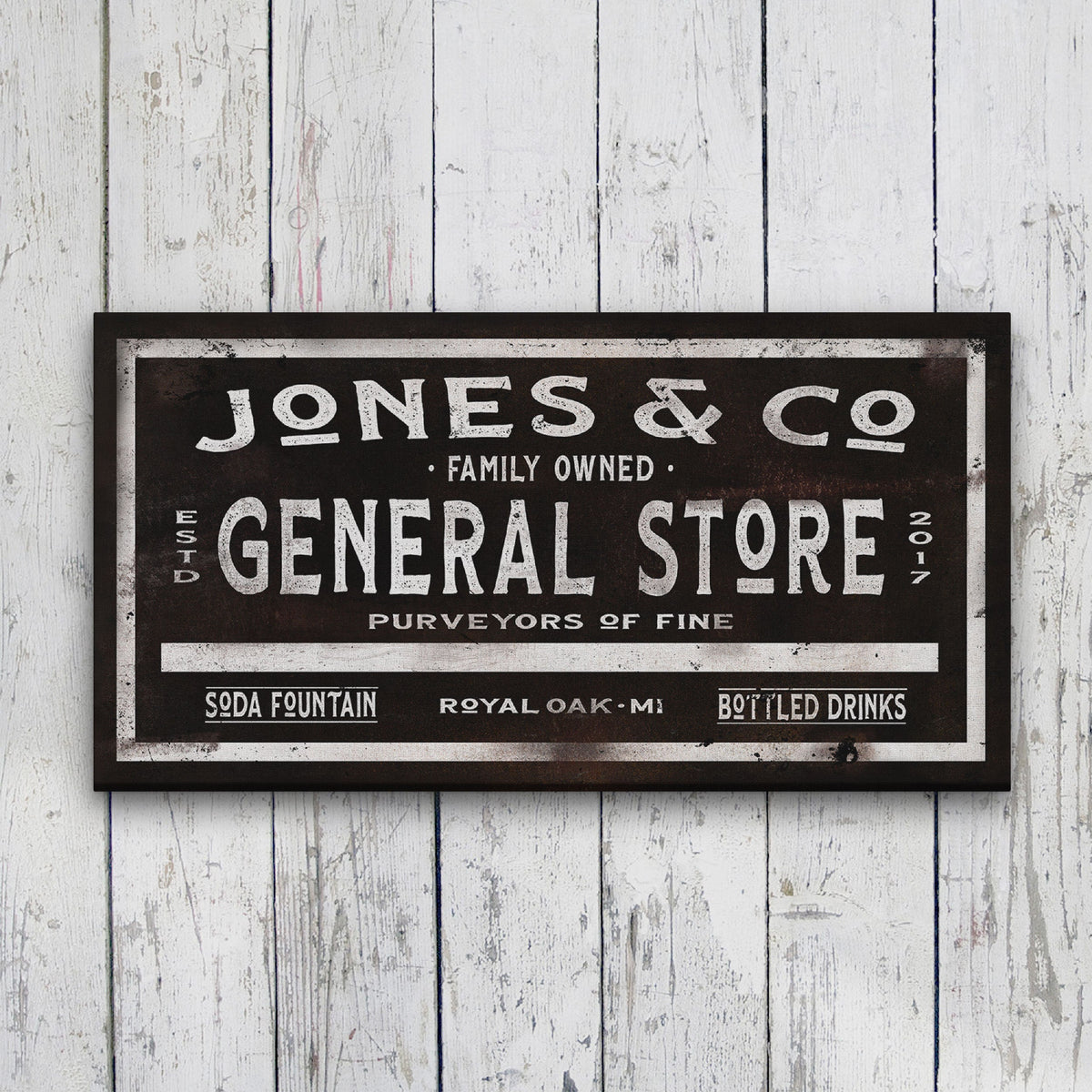 Vintage-style canvas sign with distressed black background displaying sample personalization "Jones &amp; Co" at top, "Family Owned General Store" in large letters, and "Soda Fountain Royal Oak MI Bottled Drinks" at bottom, hung on white shiplap wall