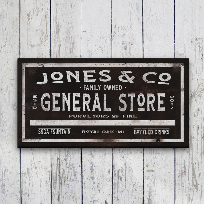 Vintage-style canvas sign with distressed black background displaying sample personalization "Jones & Co" at top, "Family Owned General Store" in large letters, and "Soda Fountain Royal Oak MI Bottled Drinks" at bottom, hung on white shiplap wall