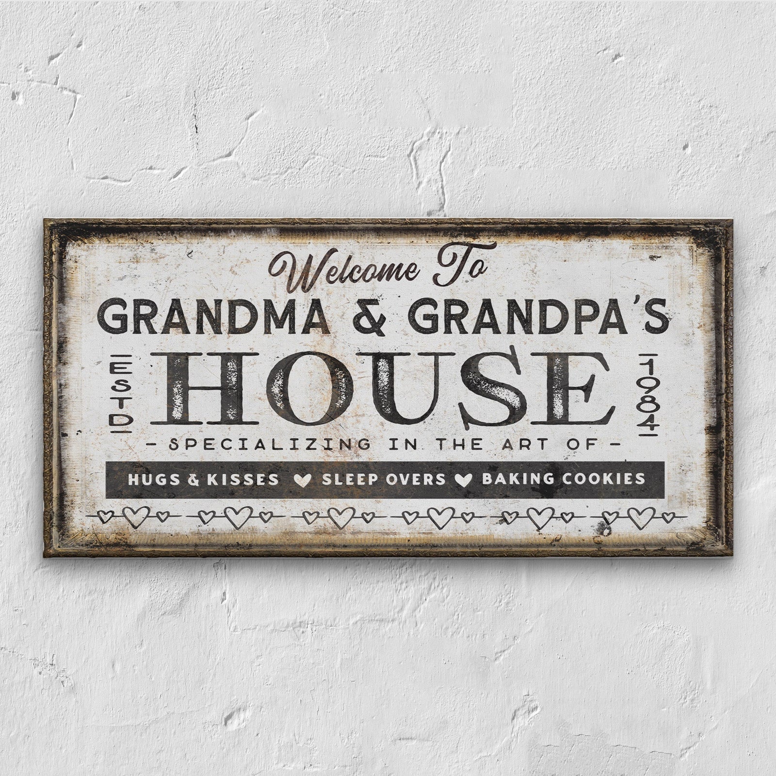 Personalized canvas sign with "Welcome To GRANDMA & GRANDPA'S HOUSE Est. 1984" in distressed cream and black vintage style, featuring heart borders and text reading "Specializing in the Art of Hugs & Kisses, Sleep Overs, Baking Cookies