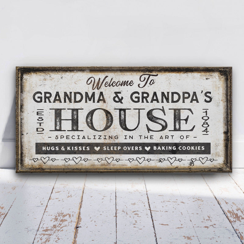 Distressed vintage canvas sign reading "Welcome To Grandma & Grandpa's House" with rustic frame and heart border, specializing in hugs, kisses, sleepovers, and baking cookies.