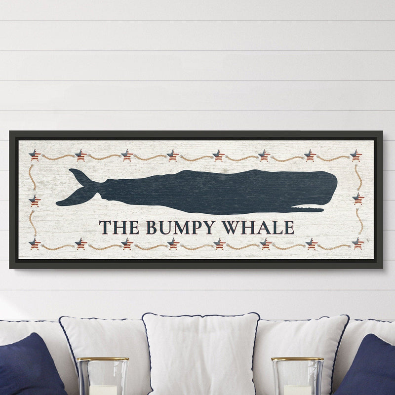 Framed canvas sign with navy whale silhouette, "THE BUMPY WHALE" text below, Americana star and rope border, black frame, displayed above a white sofa with navy pillows.