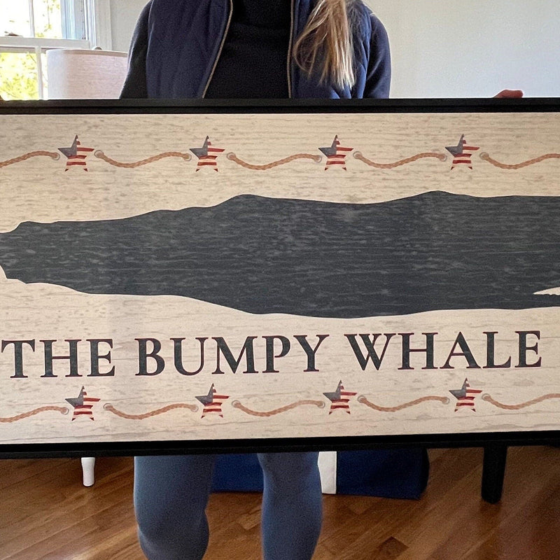 Framed canvas sign with navy whale silhouette, decorative Americana stars and rope border, distressed white wood background, and "THE BUMPY WHALE" text centered below