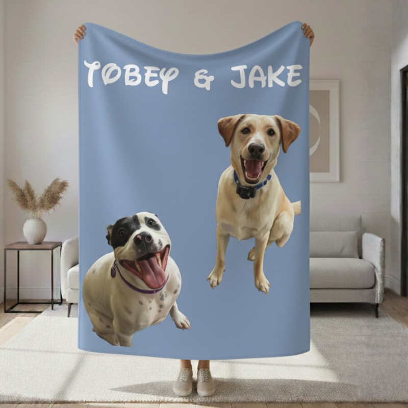 Blue sherpa blanket printed with sample names "Tobey & Jake" and cartoon portraits of two smiling dogs, displayed draped in a living room setting.