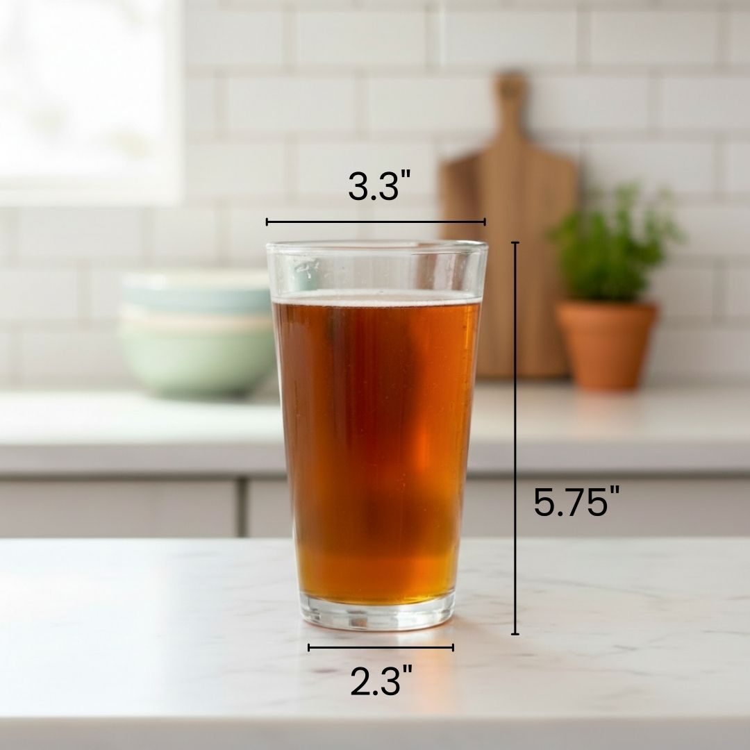 Clear pint glass filled with amber beverage, showing dimensions of 3.3 inches wide and 5.75 inches tall, displayed on kitchen counter with white subway tile backsplash