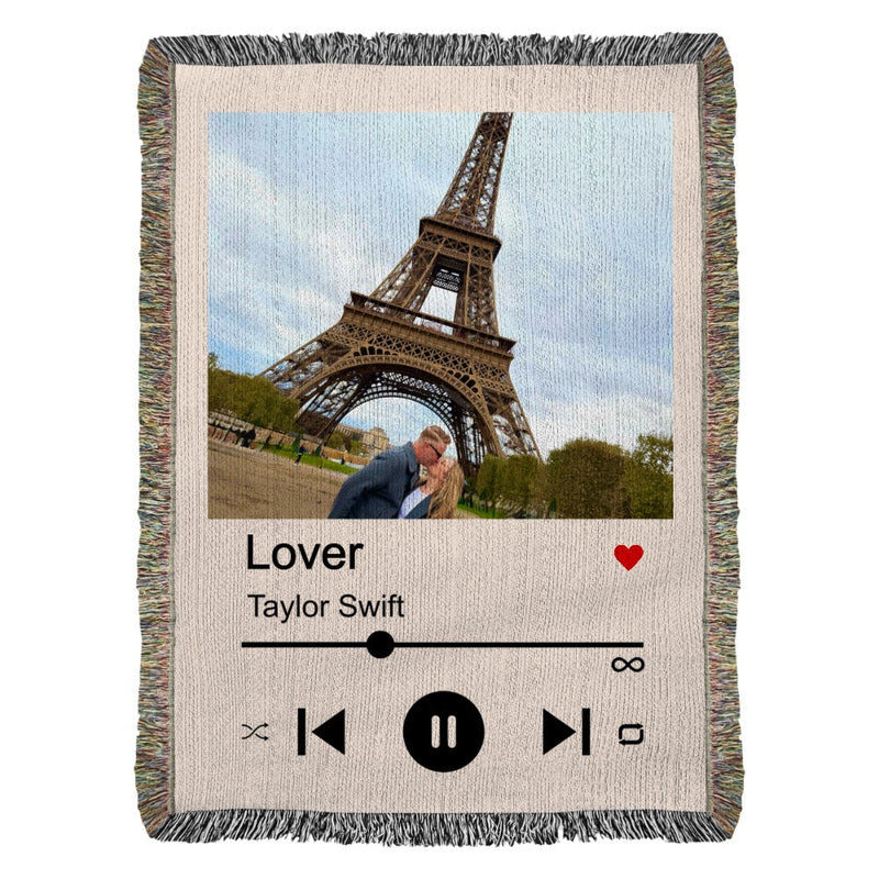 Woven blanket featuring a photo of a couple under the Eiffel Tower with "Lover" and "Taylor Swift" printed below, music player controls, and a red heart icon.