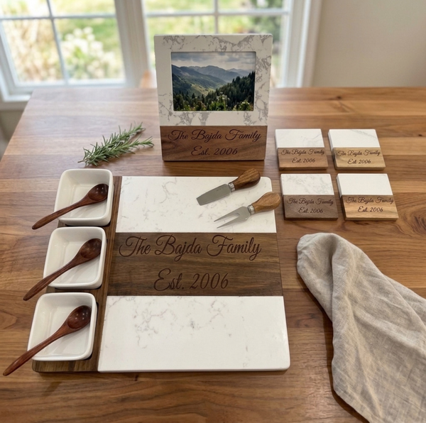 Personalized marble and acacia wood housewarming gift set: charcuterie board with bowls and tools, four coasters, and a photo frame, all engraved the The Bajda Family Est. 2006