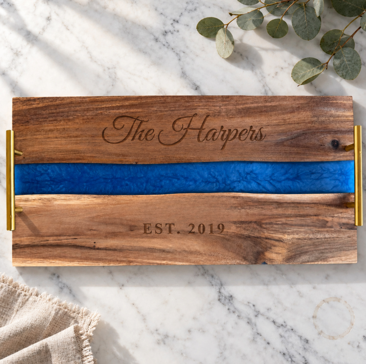 Personalized Blue River Serving Tray engraved The Harpers above a blue pearl resin river and EST. 2019 below, acacia wood with gold handles on white marble