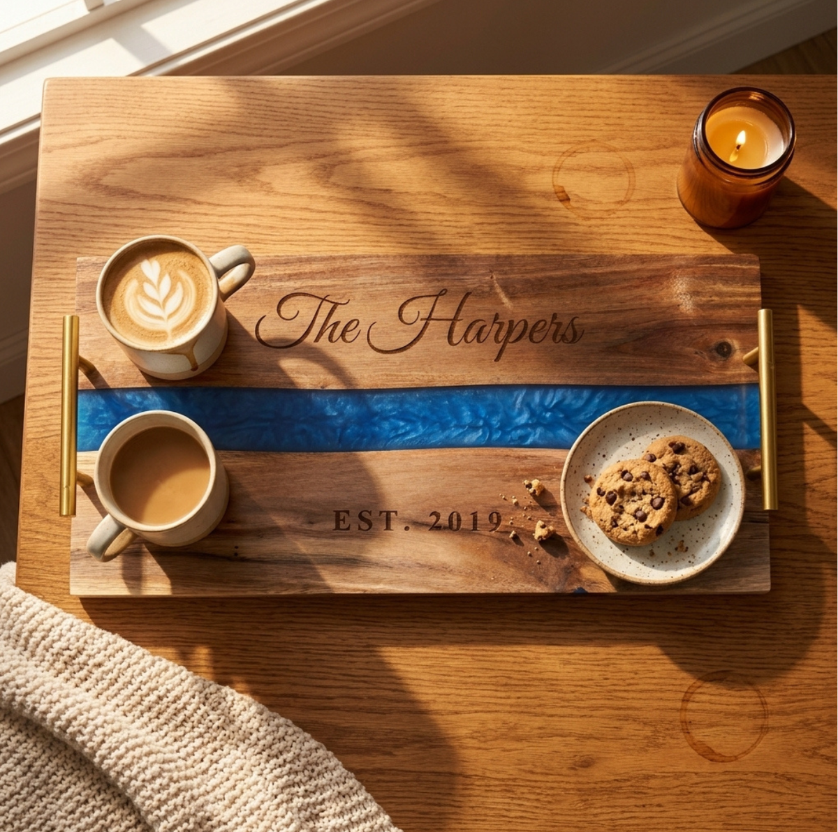 Acacia and blue resin serving tray engraved The Harpers and EST. 2019 holding two lattes and chocolate chip cookies on an oak coffee table in morning sun