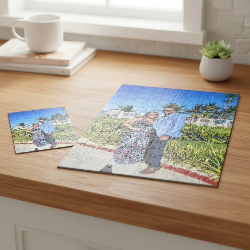Two custom photo puzzles displayed on wooden desk, larger puzzle partially assembled showing outdoor photo of two people in garden setting, smaller completed puzzle beside it