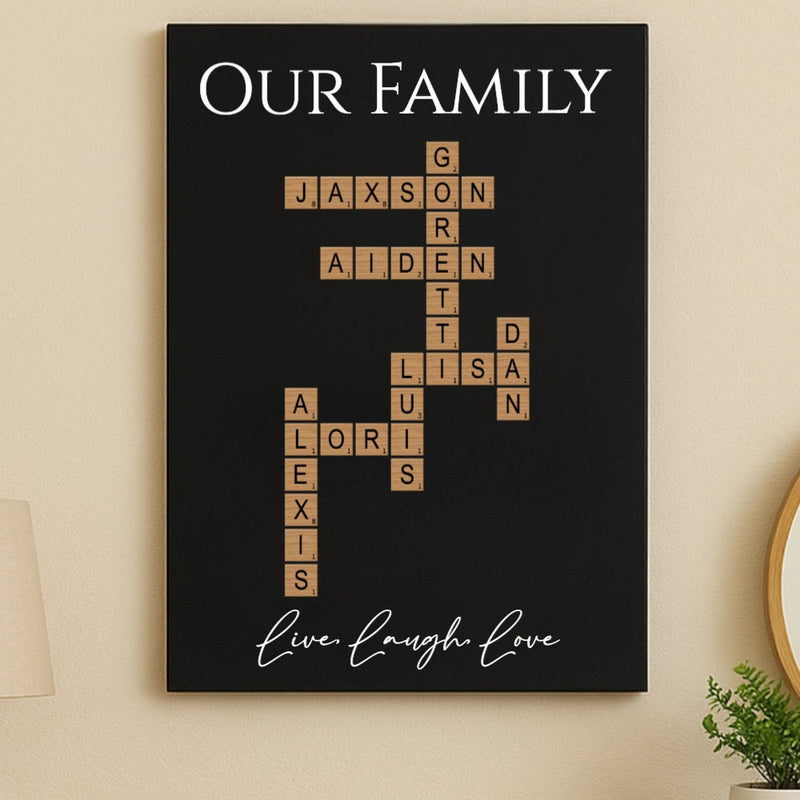 Black wood sign with "Our Family" header and Scrabble-style tiles forming a crossword with sample names Jaxson, Grayson, Aiden, Lisa, Lori, and Alexis, with "Live Laugh Love" script at bottom.