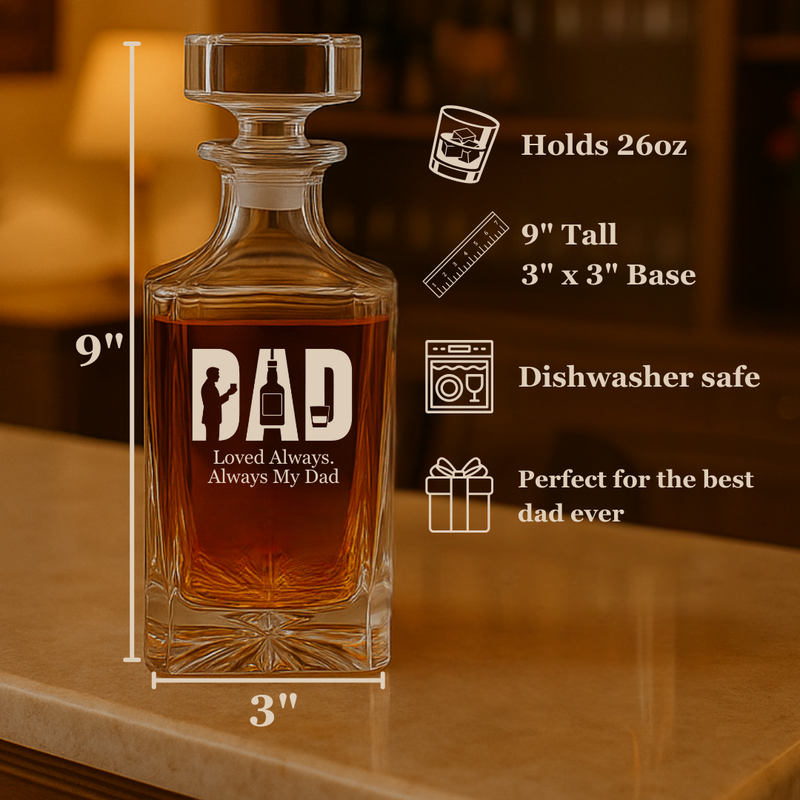 Clear glass whiskey decanter filled with amber liquid, engraved with sample text "DAD" and "Loved Always, Always My Dad", displayed on wooden surface with spec sheet showing 9" height and 26oz capacity.