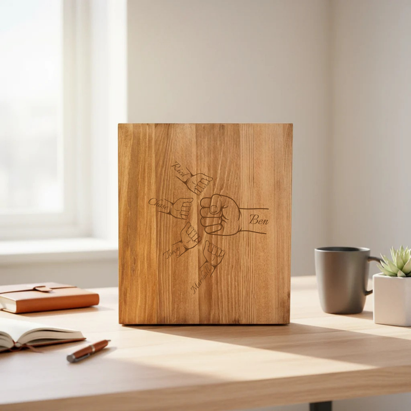 Wooden presentation box with laser-engraved fist design and sample names "Dad," "James," "Anna," "Ben," and "William" arranged in a circle around the fists