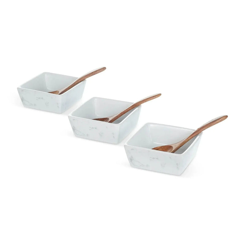 Three white marble square bowls with wooden serving spoons arranged in a row
