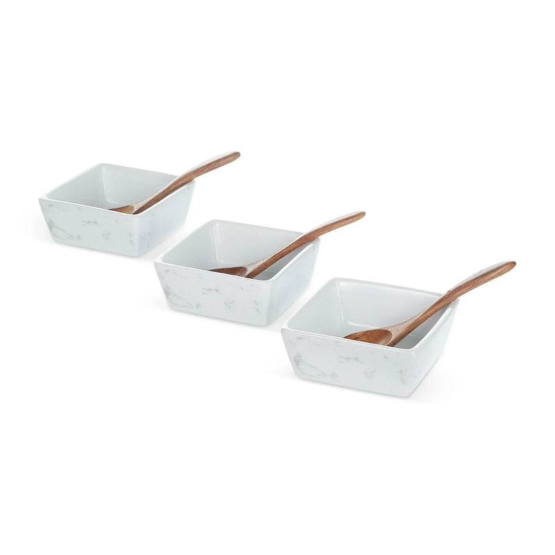 Three white marble bowls with wood handles arranged in a row, each containing a wooden spoon