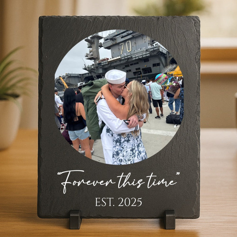 Dark slate picture frame with circular photo opening displaying a couple kissing in front of an aircraft carrier, engraved with "Forever this time" and "EST. 2025" below the image, shown standing on wooden surface