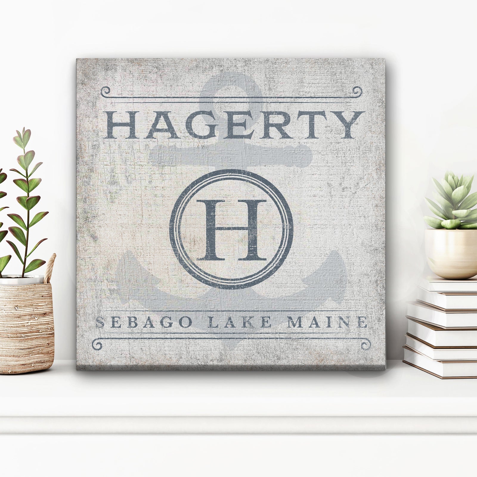 Canvas sign with personalized name "HAGERTY" at top, monogram initial "H" in circular badge, and "SEBAGO LAKE MAINE" text below on distressed white background