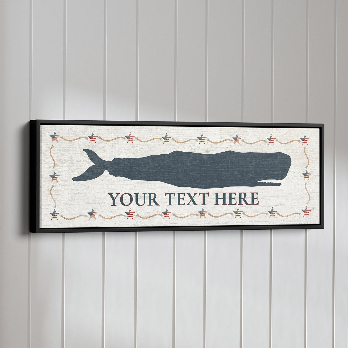 Personalized Framed Whale Canvas Sign displaying a large navy blue sperm whale silhouette above custom text on a distressed white background with an Americana star and rope border, in a black floating frame mounted on a white beadboard wall
