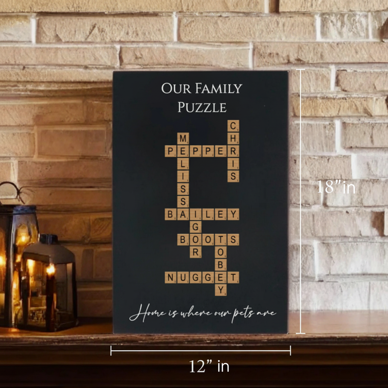 Black wall sign with sample family names "Pepper," "Melissa," "Chris," "Bailey," "Boots," "Nugget," and "Robby" arranged in crossword puzzle format with "Our Family Puzzle" at top and "Home is where our pets are" at bottom, 12" x 18