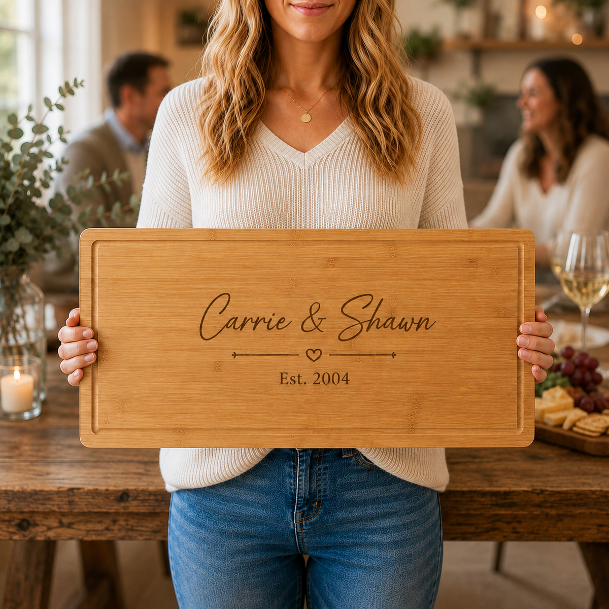 Woman holding a personalized bamboo serving board engraved with Carrie &amp; Shawn, a heart divider and Est. 2004 at a dinner gathering with friends