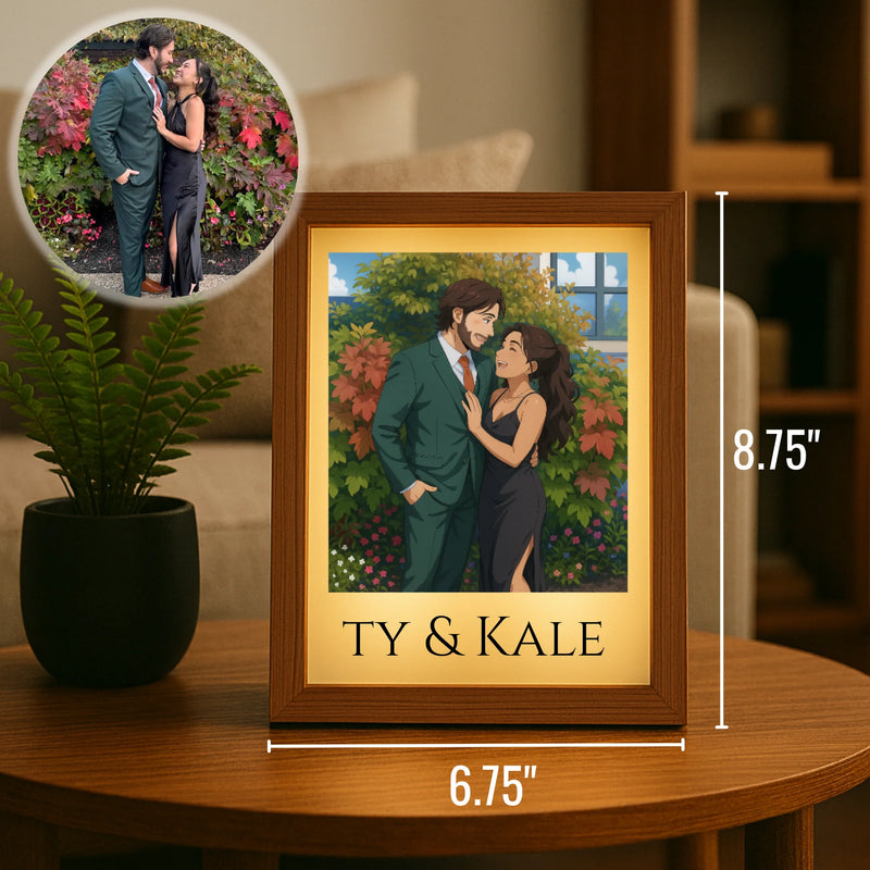 Framed anime-style portrait with sample names "TY & KALE" showing couple in garden setting, wood frame with yellow mat, displayed on table next to potted plant, measuring 6.75" by 8.75