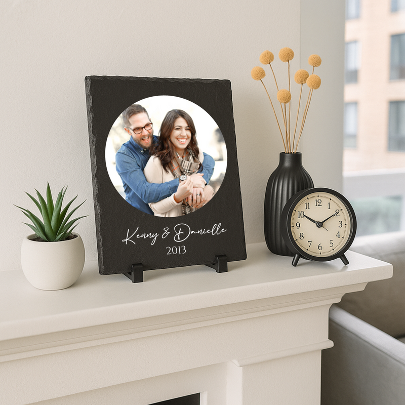 Black slate picture frame with circular opening displaying photo of couple, personalized with engraved sample names "Kenny & Danielle" and year "2013