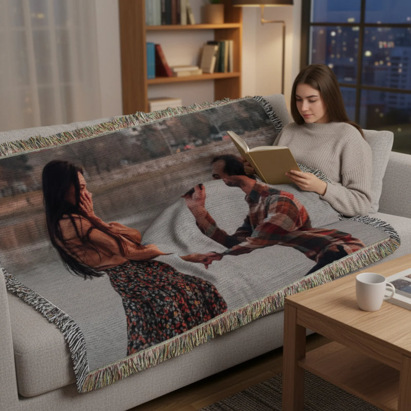 Personalized photo throw blanket draped over a sofa, displaying a woven image of two people, with colorful fringe trim along the edges.
