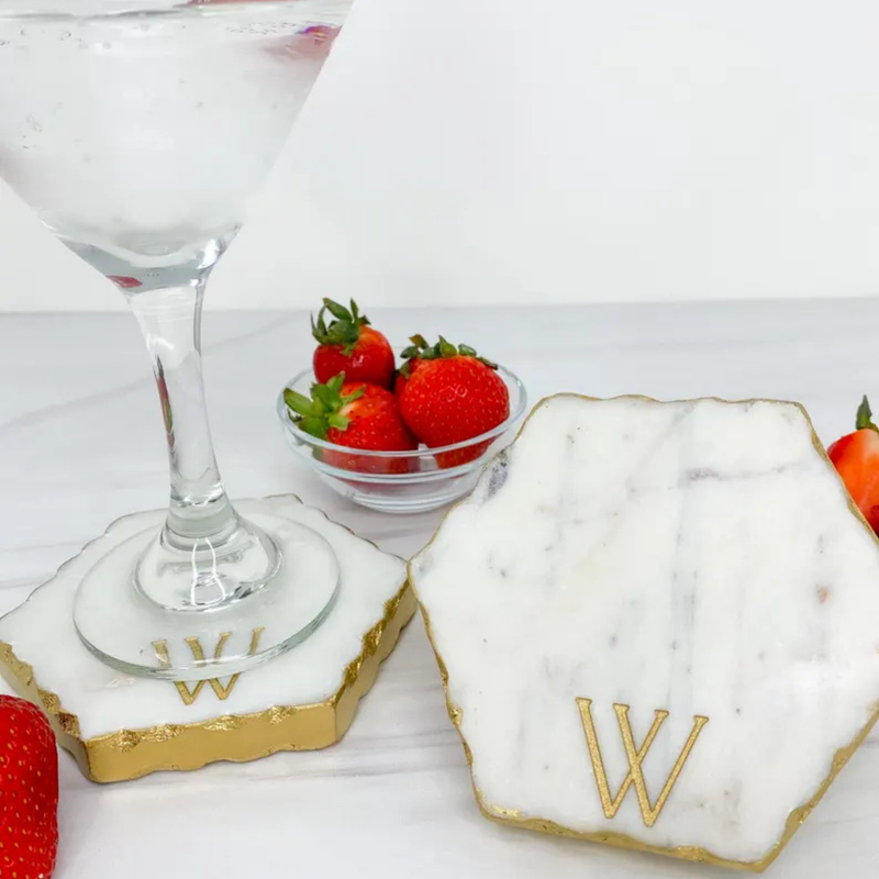 Marble charcuterie board with gold edge engraved with sample initial "W" positioned next to a cocktail glass and fresh strawberries on white surface