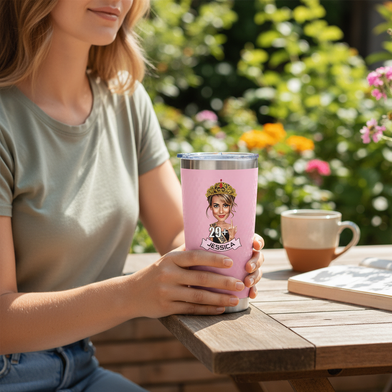 Pink stainless steel tumbler with insulated lid held by woman in garden setting, featuring sample cartoon portrait with crown, age "29" and name "JESSICA