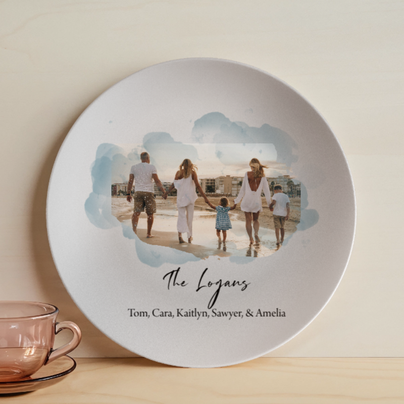 White ceramic plate featuring a beach family photo with blue watercolor frame, personalized with sample names "The Logans" and "Tom, Cara, Kaitlyn, Sawyer, & Amelia