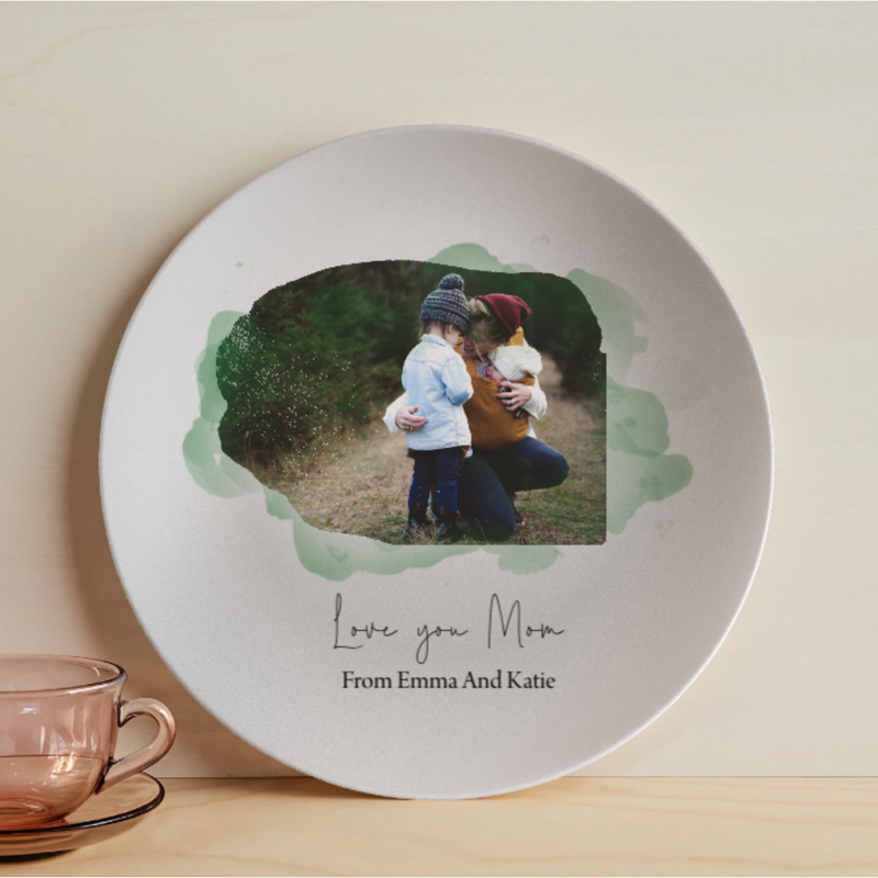 White ceramic plate with personalized photo of woman and child, surrounded by watercolor green frame, printed with "Love you Mom" and sample names "From Emma And Katie