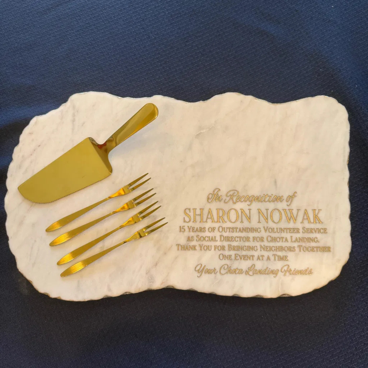 Marble charcuterie board engraved with a multi-line retirement recognition message honoring 15 years of volunteer service, styled with a gold cake server and forks. 