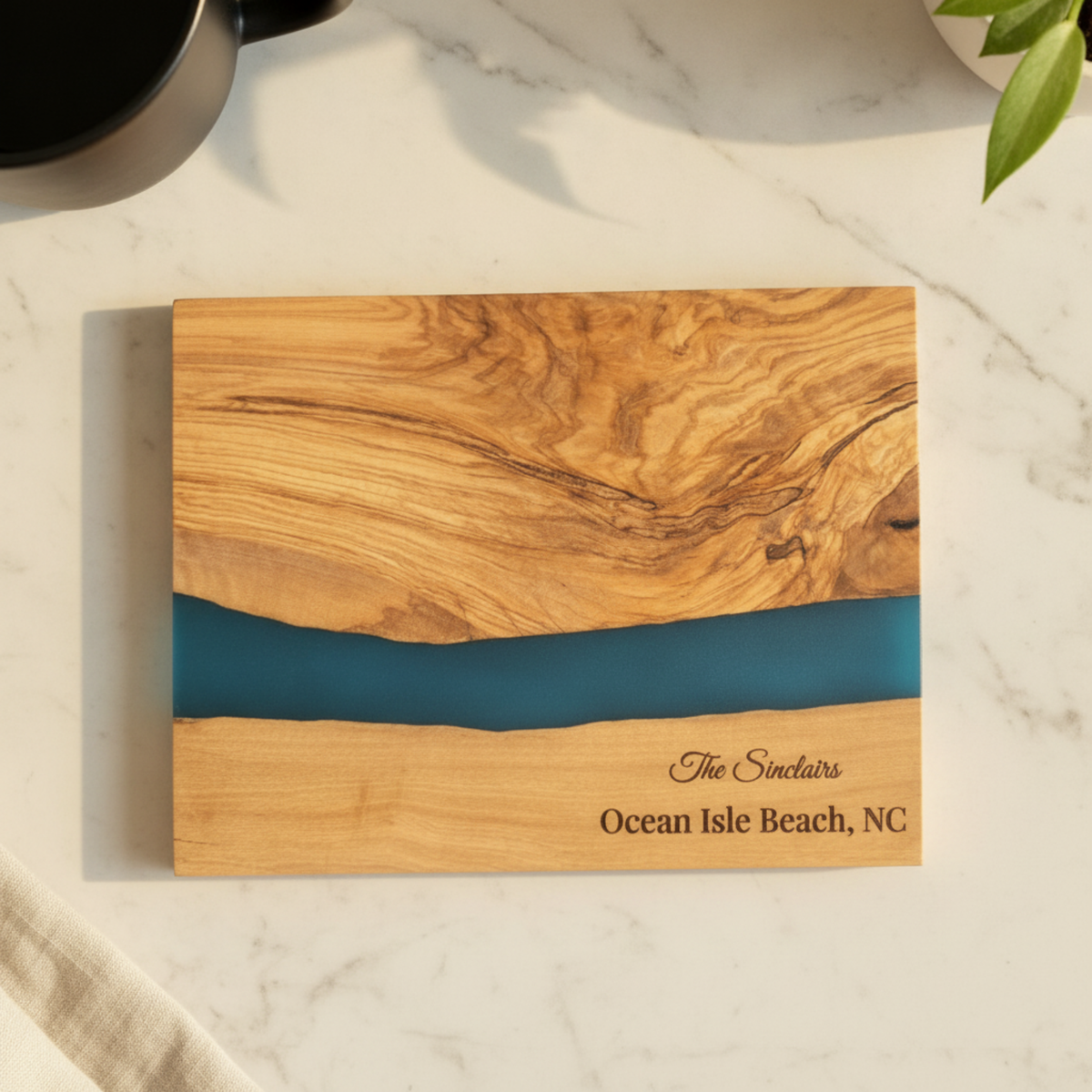 Wooden cutting board with blue resin inlay and engraved text on a marble surface.